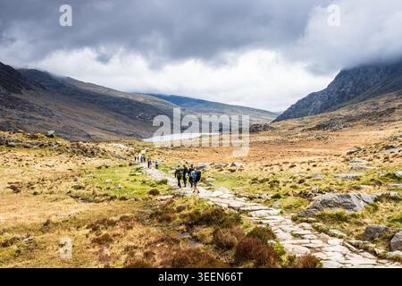 A high-angle landscape shot of a stone-paved hiking trail in the Ogwen Valley, North Wales. Multiple groups of hikers are seen trekking down the path Stock Photo