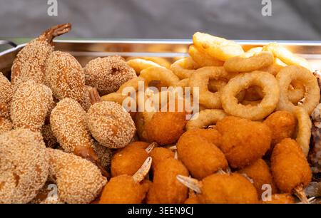Fried Asian snacks on display, featuring crispy onion rings, tempura shrimp, and assorted dumplings on food markets, street food festival Stock Photo