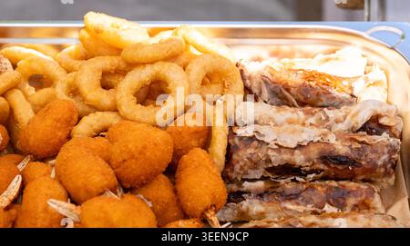 Fried Asian snacks on display, featuring crispy onion rings, tempura shrimp, and assorted dumplings on food markets, street food festival Stock Photo