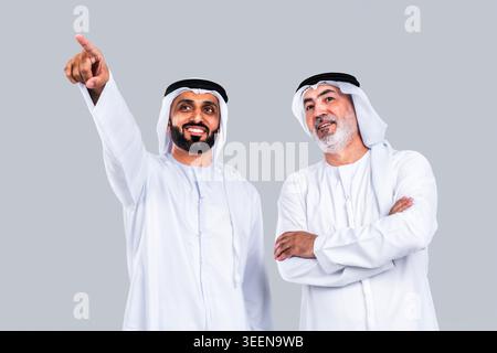 Arab men standing together looking at a specific point in the distance, with one man pointing his finger up, while the other with folded arms observes Stock Photo