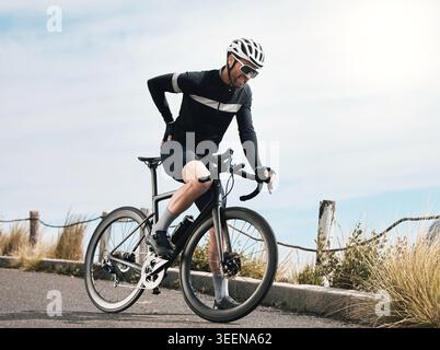 Person, cyclist and bike with back pain outdoor for bad posture, discomfort or strain. Fitness, accident and man with sore muscle, bicycle injury or Stock Photo