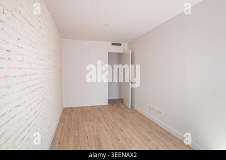 Empty room with light wooden floor and white brick wall. A door leads to another space. The room is bright and minimalistic, suitable for interior Stock Photo