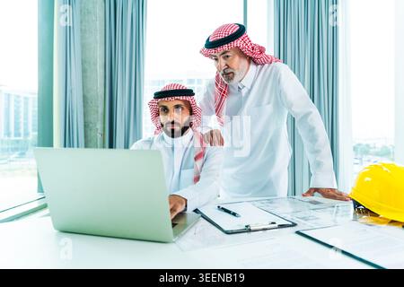 Two saudi businessmen collaborating on a new real estate project, reviewing architectural plans and discussing corporate strategy in a modern office, Stock Photo