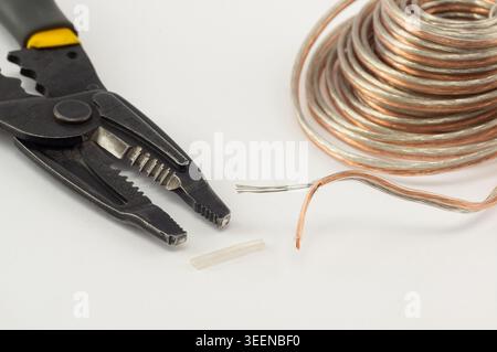 Close-up of a wire stripper tool and transparent copper speaker cable on a white background, illustrating electrical work, wiring installation, audio Stock Photo