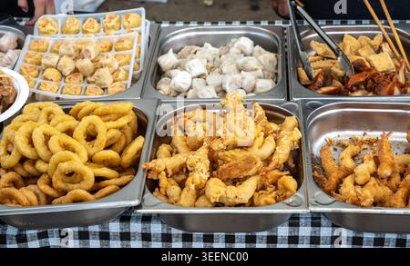 Variety of fried Asian snacks on display, featuring crispy onion rings, tempura shrimp, and assorted dumplings. Perfect for food markets or street foo Stock Photo