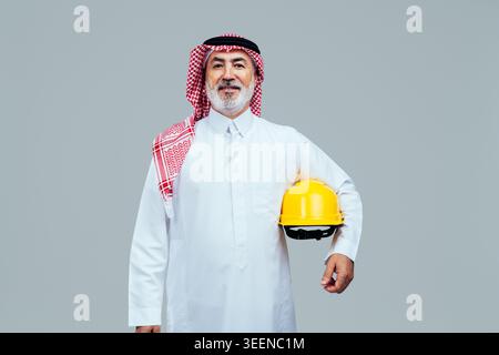 Saudi senior man engineer confidently holding a yellow hard hat, representing experience and expertise in construction, engineering, and development w Stock Photo