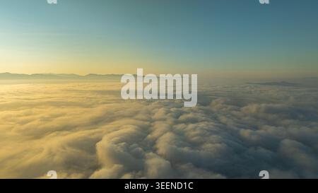 Serene aerial landscape featuring glowing morning light illuminating soft clouds and hazy mountain horizons. Ideal for travel, meditation, and natural Stock Photo