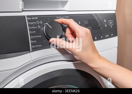 Woman turning washing machine program dial on control panel. Adult female adjusting front loading appliance settings in laundry room. Domestic cleanin Stock Photo