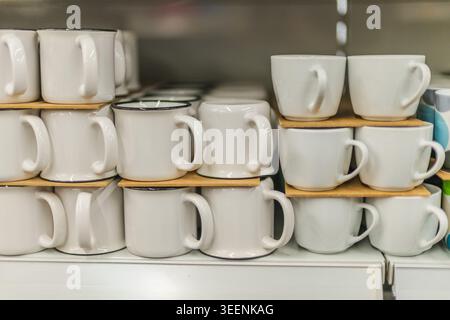 White ceramic mugs arranged on shelf in kitchenware and household goods store Stock Photo