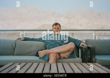 Man sitting on an outdoor sofa, enjoying relaxation with a mountain view in the resort Stock Photo