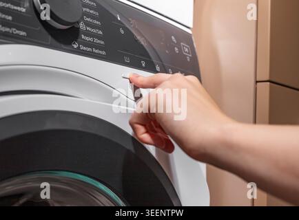Hand turning on washing machine, launching laundry, pressing button with finger. Stock Photo