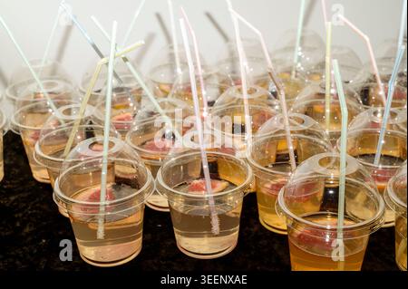 Fresh red beverage in takeaway plastic glasses with straws outdoors on a sunny day. Greenery bokeh. Concept of open air festival, relaxed youth lifest Stock Photo
