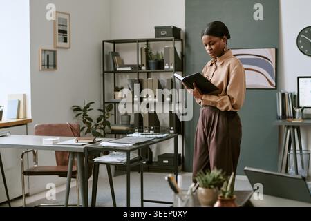 Black Adult Woman Reviewing Documents in Modern Office Workspace Stock Photo