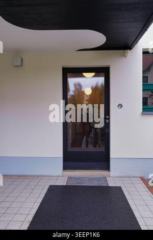 The minimalist entrance of Haus Rabe in Zwenkau, a Bauhaus modernist masterpiece featuring an illuminated glass door and sleek canopy Stock Photo