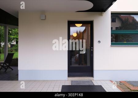 The minimalist entrance of Haus Rabe in Zwenkau, a Bauhaus modernist masterpiece featuring an illuminated glass door and sleek canopy Stock Photo