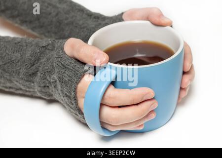 Side view of human hands in a grey knitted sweater holding a large blue ceramic mug with black coffee isolated on a white background Stock Photo