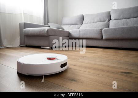 Robot vacuum cleaner cleaning wooden floor in modern living room Stock Photo