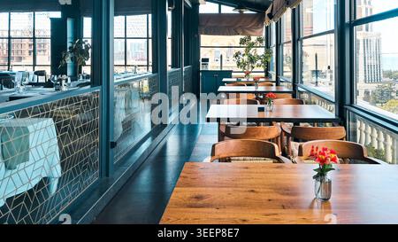 Stylish restaurant terrace with panoramic windows, wooden tables, and city views Stock Photo