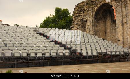 Empty white rows of seats in the Crekvina outdoor amphitheater in Kastav, Croatia. Historic ancient stone arch and ruins in the background. Stock Photo