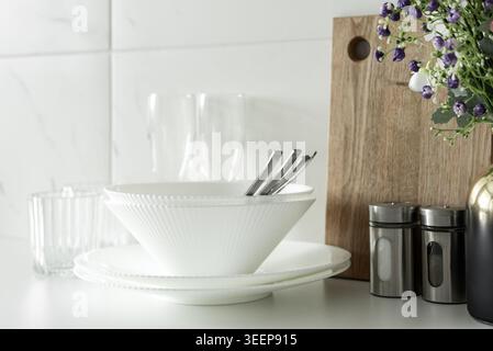 White bowls and plates with flowers and kitchen accessories in clean modern kitchen interior. Stock Photo