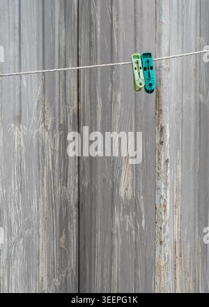 Two pegs hang quietly on a washing line in Ipoh, Malaysia, set against the textured backdrop of a weathered grey shop shutter. Stock Photo
