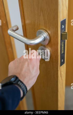 Close-up of a brass padlock securing a rusty iron hasp on an old wooden door. The contrast between the weathered metal latch and the polished lock Stock Photo