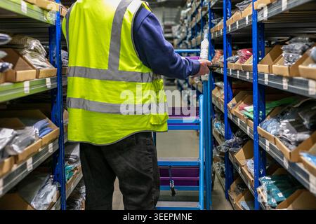 Warehouse worker using a handheld RF scanner to instantly read barcodes on bin locations or items, providing real-time data while picking Stock Photo