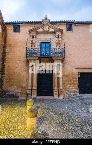 Ornate stone doorway with columns and a wrought iron balcony adorn the facade of a historic building on a cobblestone street in Ronda, Andalusia, Spai Stock Photo