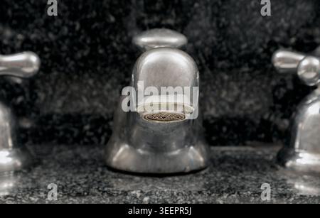 a central silver spout rises with sculptural strength from a backdrop of dark, textured stone. Its rounded form remains in sharp focus, while the flan Stock Photo