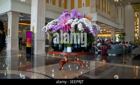 Stunning floral centerpiece with white and purple orchids in black ceramic pots on a round wooden table in a grand marble lobby. Colorful feathers, to Stock Photo