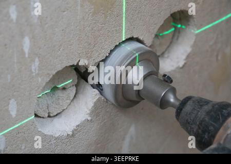 Power tool with an industrial crown drill bit carving a precise hole into a thick concrete wall, guided by bright green laser lines ensuring accuracy Stock Photo
