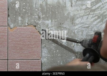 Worker using a powerful jackhammer to chip away and remove old ceramic tiles from a rough concrete bathroom wall during a home renovation and demoliti Stock Photo