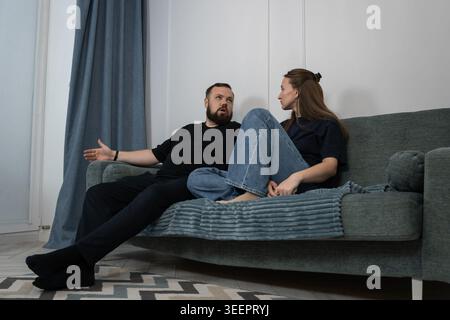 Happy couple sitting comfortably on a sofa at home, engaging in conversation and smiling, reflecting moments of togetherness, happiness and companions Stock Photo