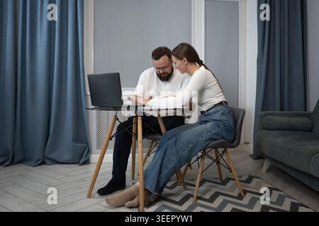 Young couple collaborating on a project, using a laptop and documents while working from their modern home office, symbolizing teamwork and shared res Stock Photo