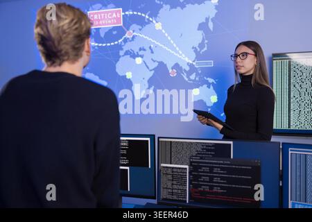 Team collaborating in a SOC monitoring critical cybersecurity events on a world map Stock Photo