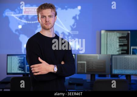 Confident cybersecurity analyst poses in front of data systems with extended monitors Stock Photo