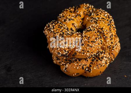 Braided simite with sesame seeds, ready-made simite from the oven lies on a black stone tray and demonstrates the embossed shape of the dough. Stock Photo