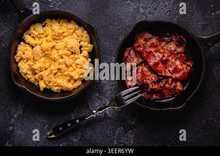 Cooked scrambled eggs and fried bacon in portion pans, top view. Stock Photo