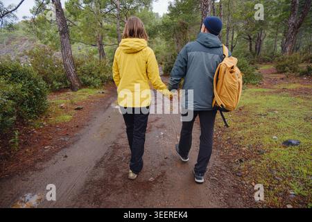 Couple enjoys Turkish coastline near Kemer. in pine forest. Sitting on stones, watching sea waves, relaxing together, slow romantic moment near calm blue water under soft winter light. Stock Photo