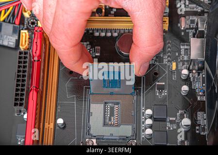A person's fingers install a central processing unit into the socket of a computer motherboard. Stock Photo