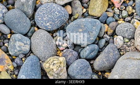 Overhead shot showcases pebbles variety, highlighting smooth, detailed rock texture. Coastal design idea with earthy color palette. Grainy surface, id Stock Photo