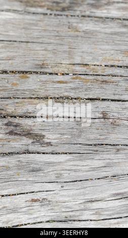 Close-up shows worn wooden planks, bleached gray with age. Texture exhibits cracks and small stones lodged between. Neutral, muted color palette ideal Stock Photo