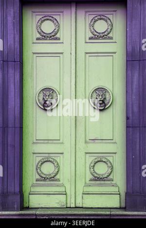 A vibrant light green wooden double door features ornate lion-head knockers and decorative wreaths. Framed by a bold purple stone portal, this archite Stock Photo