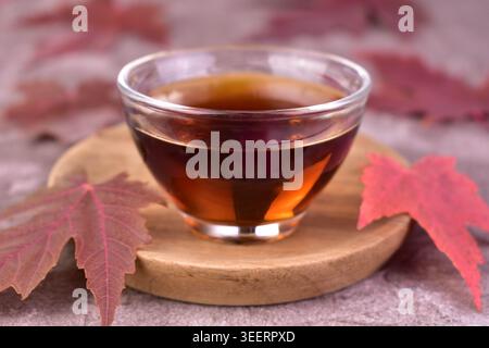 Maple syrup in a small glass bowl on a wooden tray. Close-up. Stock Photo