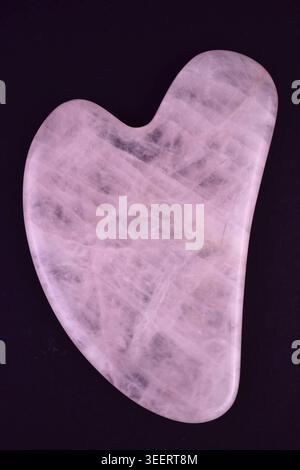 Gouache scraper for facial massage made of rose quartz on a black background. Close-up. Stock Photo