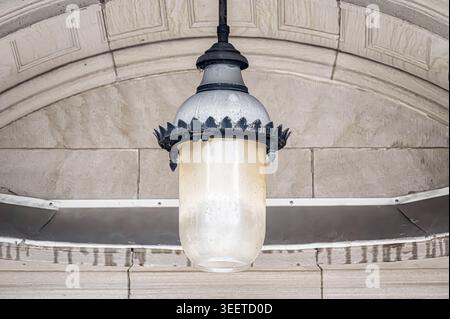 Vintage hanging lantern under stone archway, with frosted glass shade and decorative metal trim showing age and patina. Stock Photo