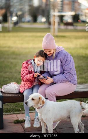 Mother and daughter using smartphone with dog in park Stock Photo