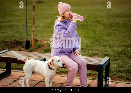 Woman drinking water with dog in park Stock Photo