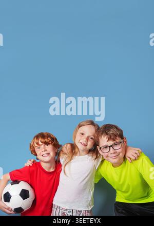 Laughing children with the soccer ball have fun, isolated on blue background. Poster with copy space. Stock Photo