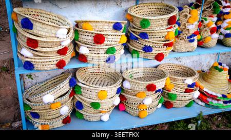 Display of handmade braided wicker baskets decorated with colorful pompoms, presented on typical blue shelves in a Moroccan souk. Stock Photo
